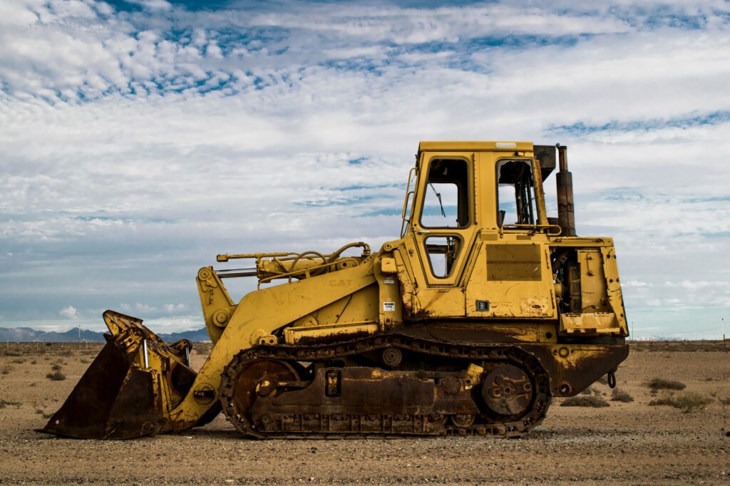 Abandoned rusty bulldozer parked in a serene desert landscape under a cloudy sky.